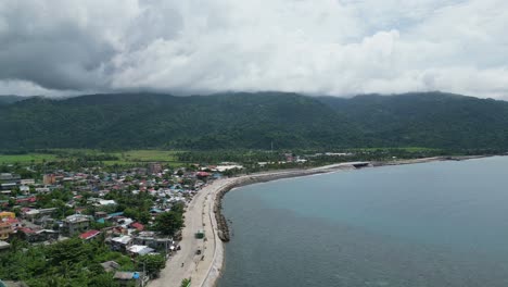 aerial, rising shot of wide bay and seawall near coastal town of virac, catanduanes, philippines, asia with mountains in background