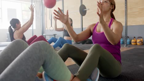 unaltered diverse women group training in pairs with medicine balls at gym, slow motion, copy space