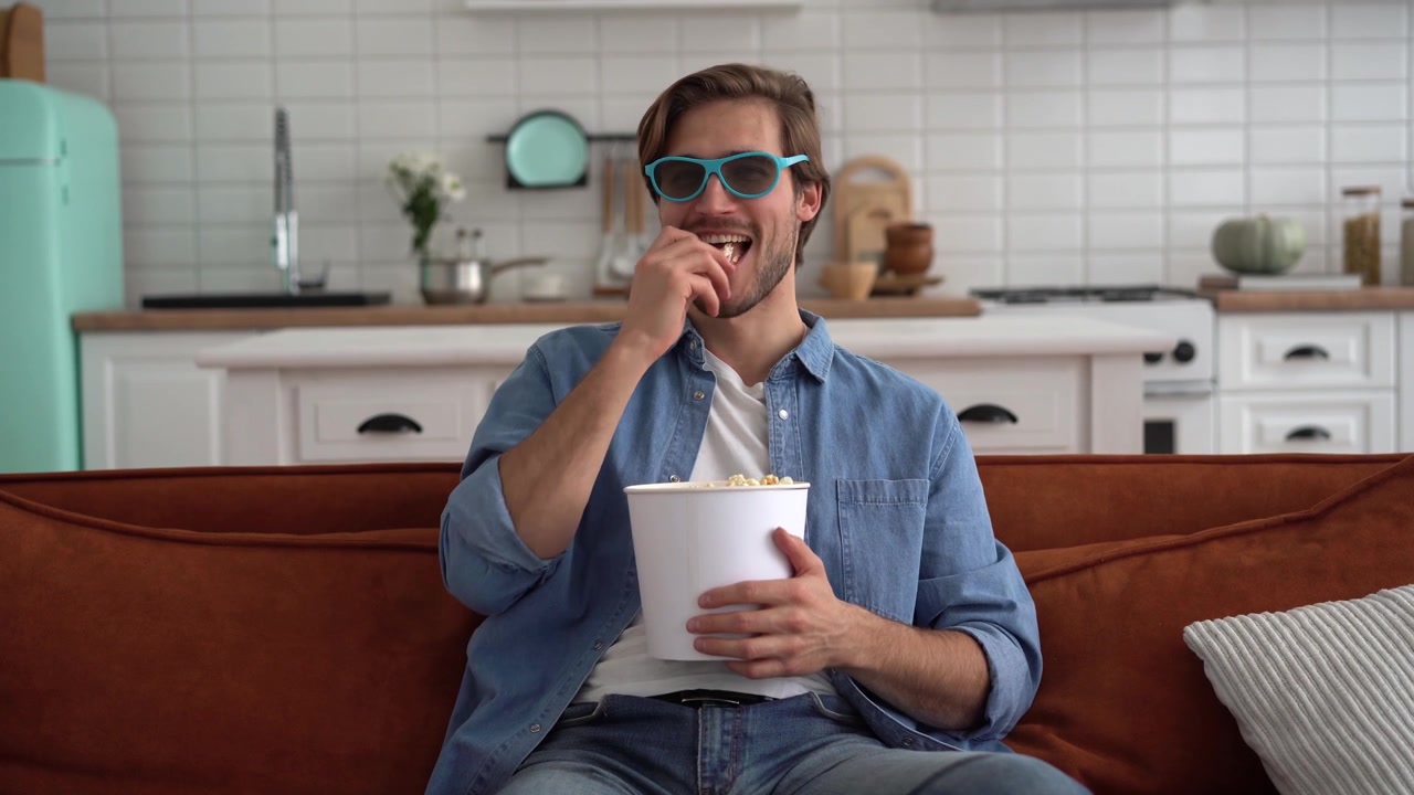 Giovane uomo che indossa occhiali 3D e mangia popcorn sul divano