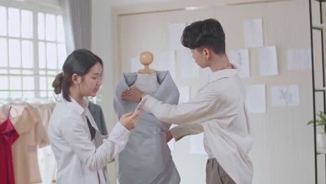 two young asian fashion designers adjusting fabrics on a tailored mannequin