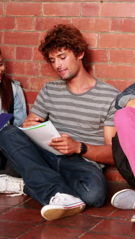 estudiantes sentados contra la pared leyendo libros de texto