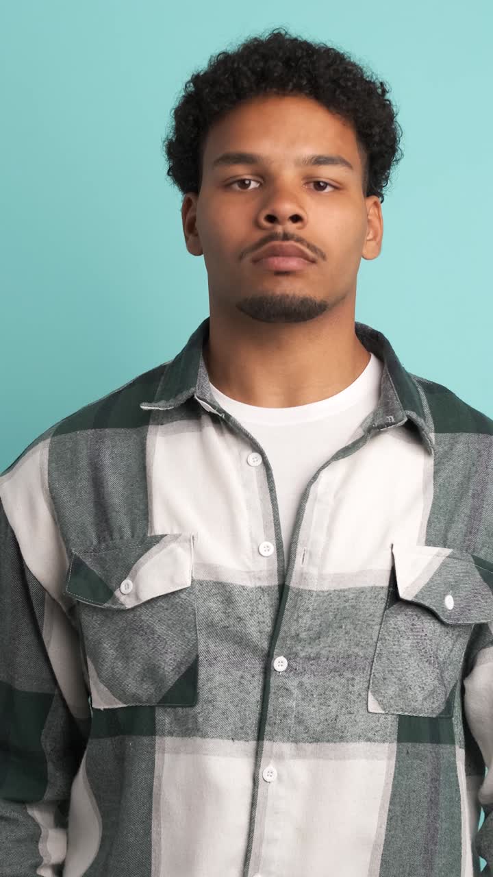 Serious young man looking at camera in blue studio