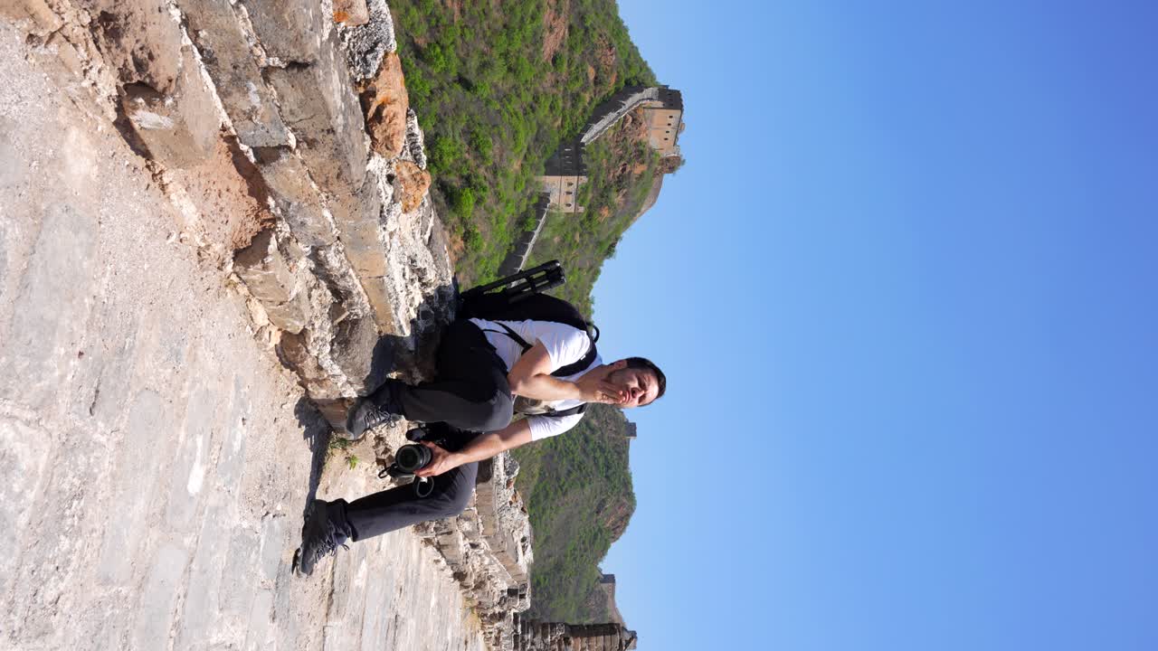 Tired photographer resting on stone steps of Great Wall in Jinshanling, China. Vertical