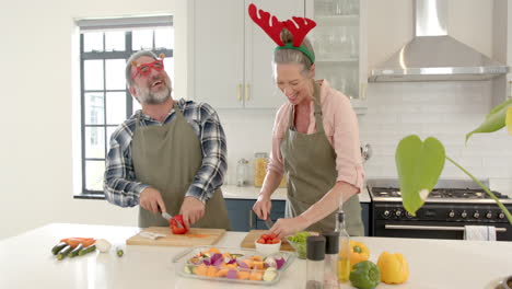 at christmas, mature couple wearing festive accessories preparing vegetables in modern kitchen