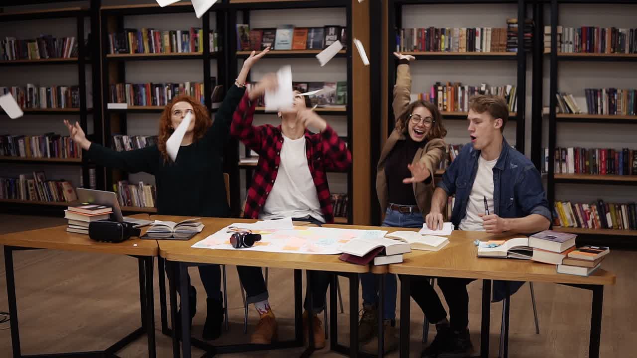 Slow motion of students throwing the sheets of paper up after hours of studying in uni library. Happy and free students who don't want to study or are celebrating the start of vacations, starting to dance