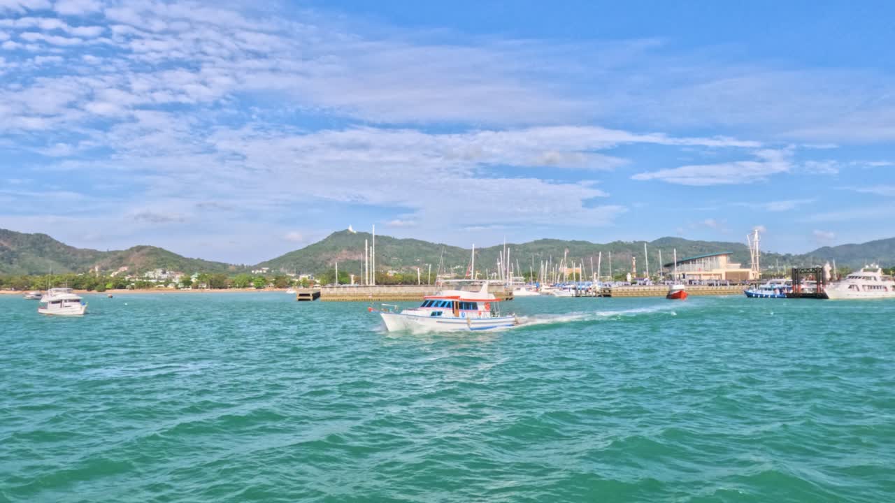 Boats navigate the vibrant waters of Rawai Beach, Phuket under clear skies, capturing a lively coastal scene