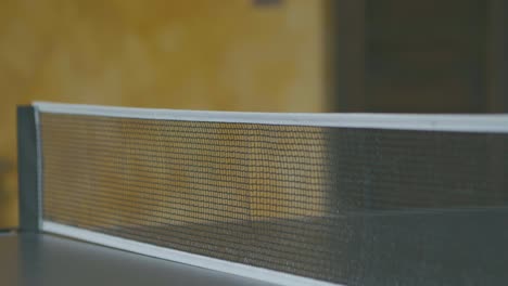 slow motion of a ping pong ball hitting the net during a match, detail of the net while the rest of the table is out of focus