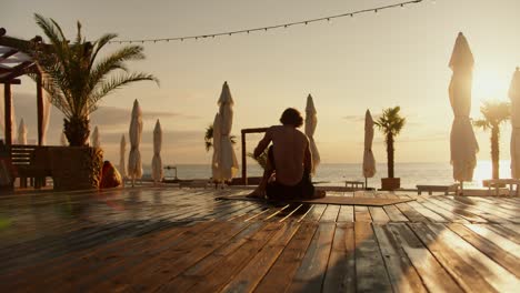 overview on a yogi guy who is sitting on the beach at sunrise. morning beach, harmony of body and mind