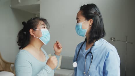 asian female nurse and patient wearing face masks talking and looking to camera in hospital