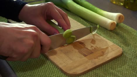 CU-Male-Chef-preparing-fresh-leeks,-chopping-them-with-a-sharp-knife-to-create-a-dish