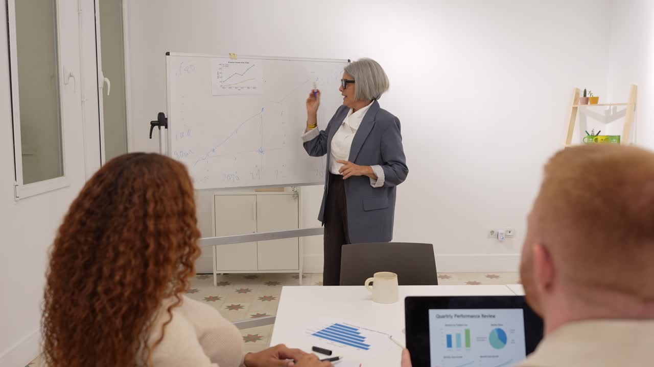 Imprenditrice senior spiega i grafici sulla lavagna ai colleghi