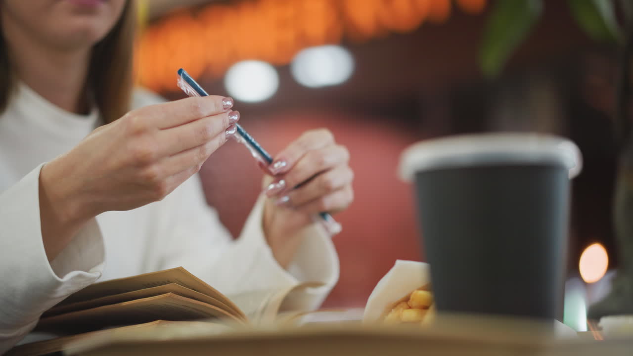 Close-up of woman examining a blue straw in a modern restaurant setting with a blurred background featuring a drink cup, fries, and vibrant lighting
