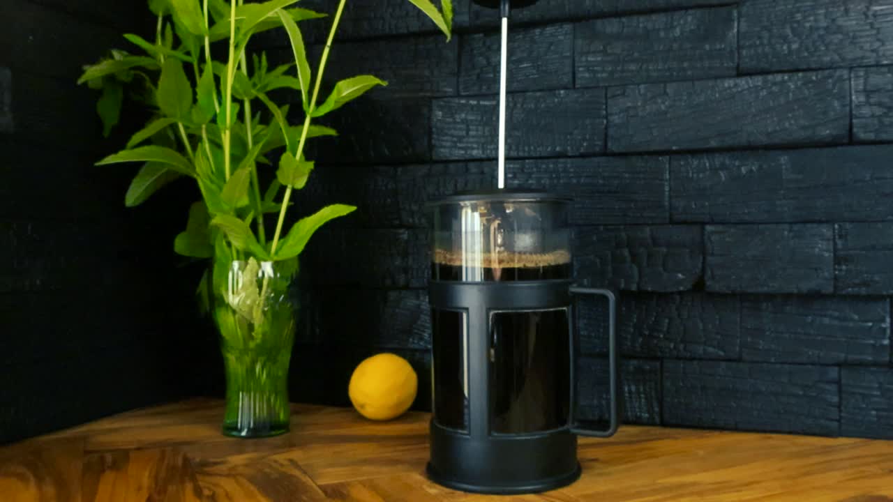 Gorgeous closeup or close up footage of a french coffee cup or a press can on an olive wood table with lemon and mint plants by its side. Yakisugi burnt and charred black wood panels in the background