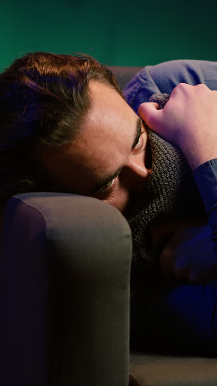 Vertical video Man laying down hugging pillow watching TV, heartbroken by upsetting movie plot