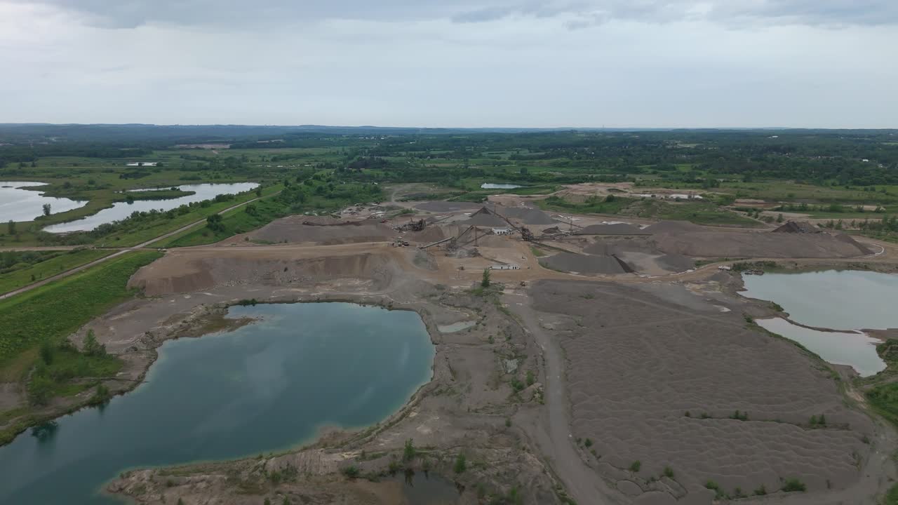 Drone establishing aerial of industrial gravel pit site with industrial terrain and water filling low spots