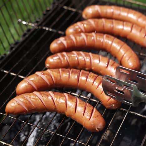 Hot dog sausages roasting in smoke. Chef opens grill grate and turns over juicy sausages. Delicious food for picnic in summer. Eating in nature