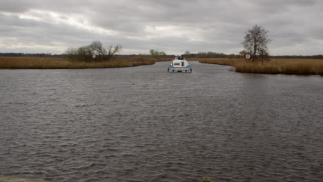 wide-shot-of-a-white-Norfolk-Broads-cruiser-boat-turning-off-the-river-bure-to-South-Walsham-Broad