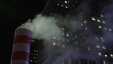 condensation cloud vapor steaming from orange white manhole pipe vent in nighttime new york city