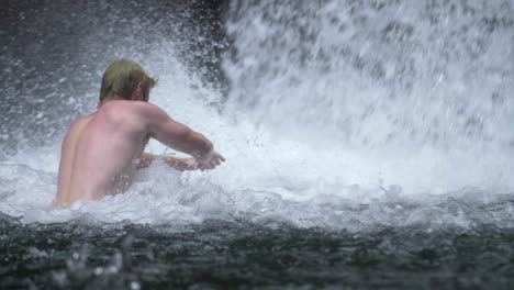 man swimming under a waterfall