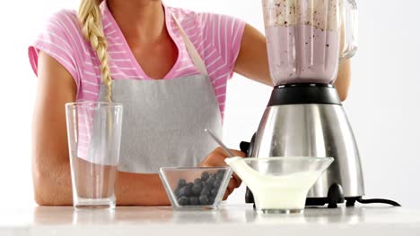 mujer preparando un batido contra un fondo blanco