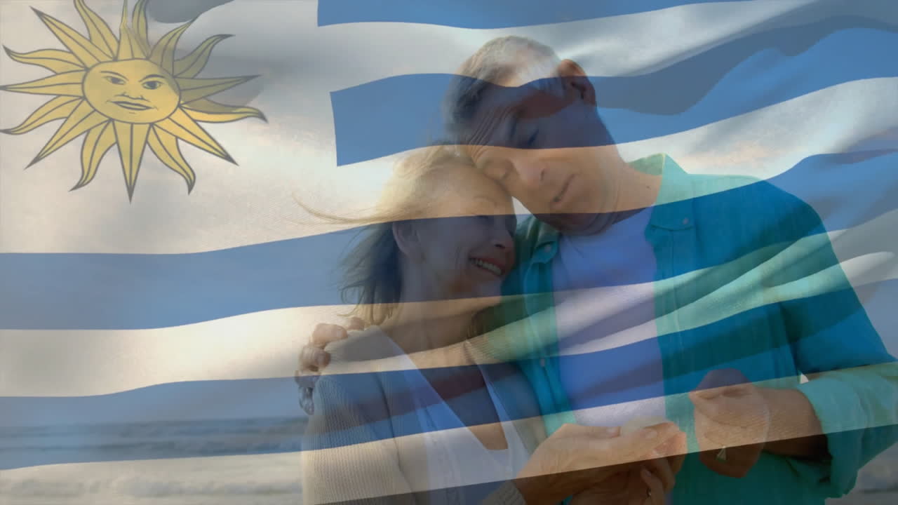 Embracing on beach, elderly couple with Uruguay flag animation overlay