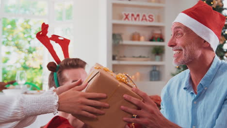 multi-generation family celebrate christmas at home wearing santa hats and antlers opening presents