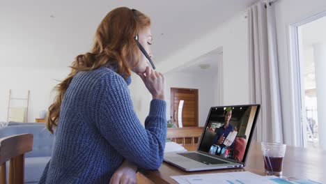 mujer caucásica usando portátil y auriculares de teléfono en videollamada con un colega masculino