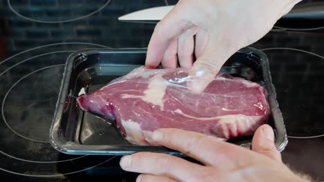 Hands-cut-open-plastic-wrapping-of-entrecote,-laying-the-fresh-raw-meat-on-top-of-the-packaging