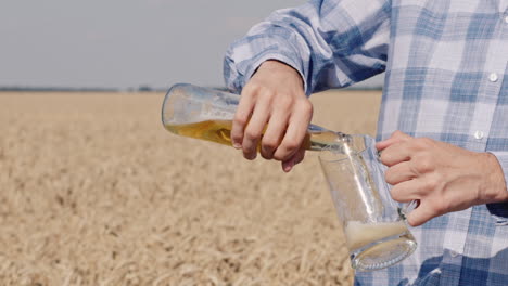 a man pours beer into a mug against the background of a field of ripe wheat