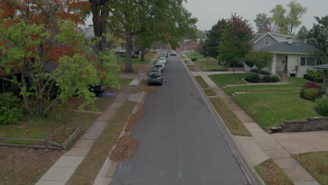 Vista-Aérea-De-Un-Coche-Que-Conduce-Por-La-Calle-Hacia-La-Cámara-En-Un-Barrio-Suburbano-En-Un-Día-De-Otoño