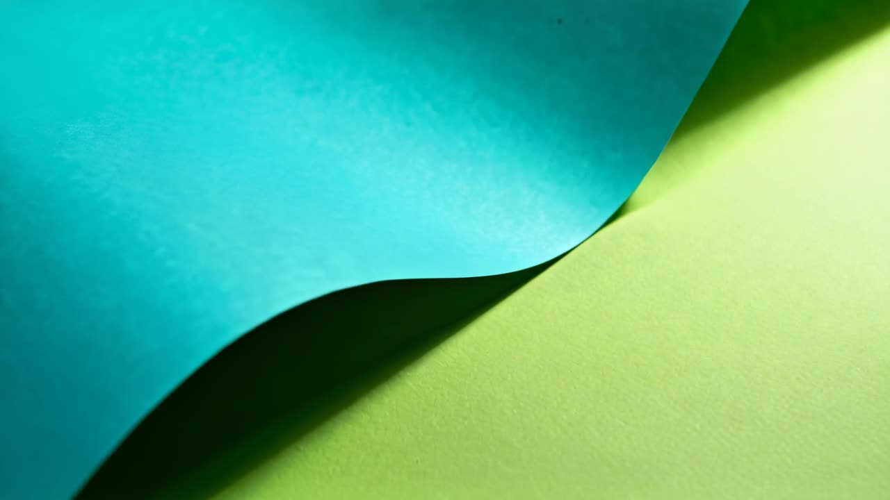 Starting teal sheet lifting, curling and sliding on table, revealing back with lime sheet in light