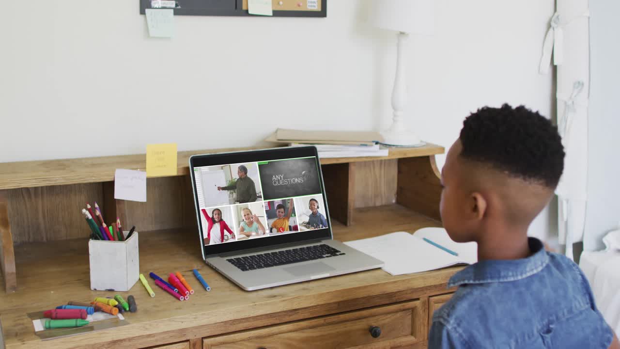 Schoolboy using laptop for online lesson at home, with diverse teacher and class on screen
