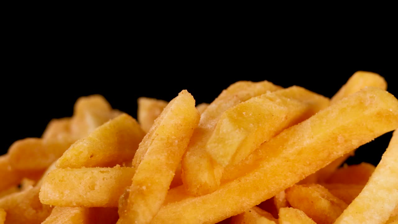 Close-up of hand picking golden French fries, dramatic lighting, rotating camera, black background