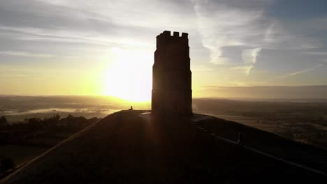 Aufsteigende-Luftaufnahme-Von-Menschen,-Die-Bei-Sonnenaufgang-Den-Glastonbury-Tor-Hinaufgehen