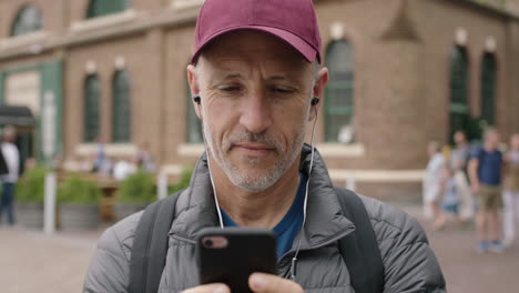 portrait of mature attractive caucasian man using smartphone social media app wearing earphones listening to music media on urban city background