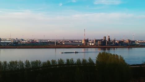 cargo ship cruising on river by industrial area, drone lowering shot