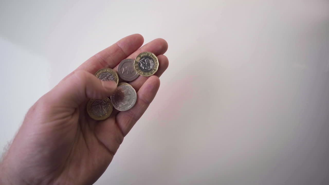 anverso y reverso de cinco piezas de monedas de una libra británica en la mano sobre fondo blanco - disparo en ángulo alto