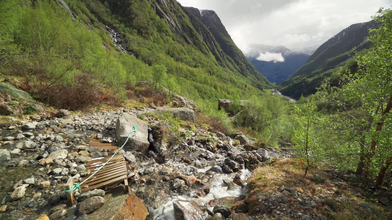 The foothills of the Buarbreen glacier in the Folgefonna national glacier park near Odda, Norway. A shallow stream rushing into the lush valley below. Dark mountains tower on the horizon