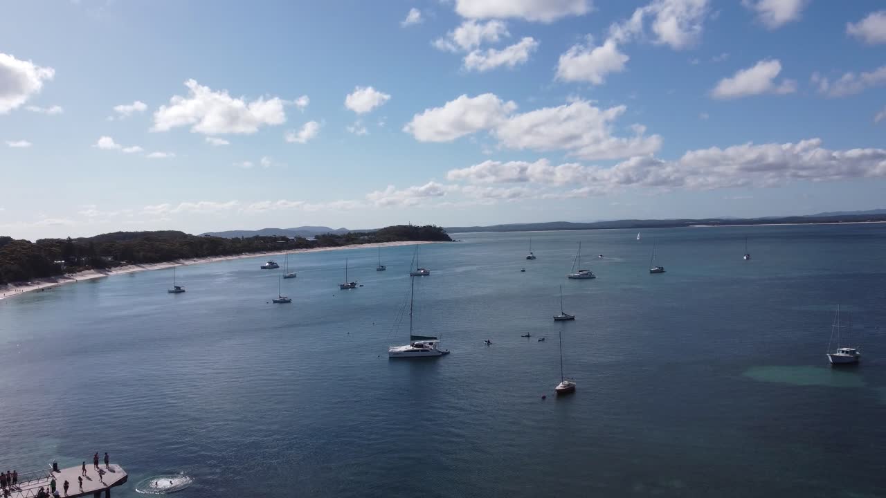 vista aérea de personas saltando de un muelle y volando sobre barcos de vela cerca de la costa
