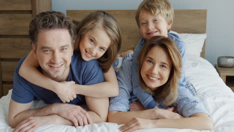 close-up view of cheerful parents and their sons lying on the bed and smiling at camera in the morning