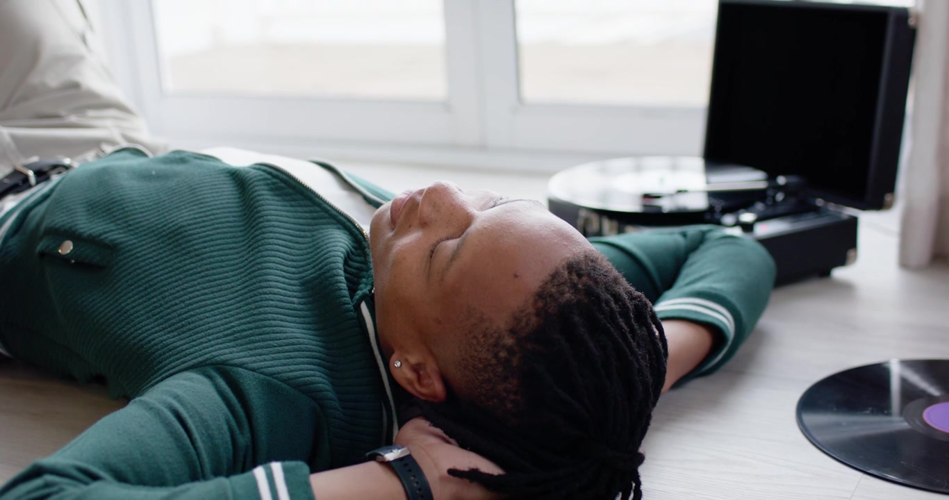 African American man lying on floor near window bathing in sunlight resting by turntable records