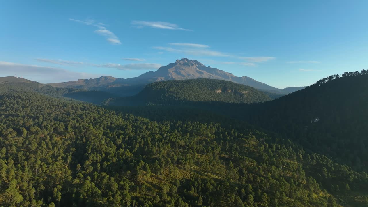 Smooth side‑to‑side drone pass over dense forest and rolling hills spotlights Iztaccihuatl volcano in clear 8 a.m. light—versatile establishing clip for travel, nature or marketing edits.