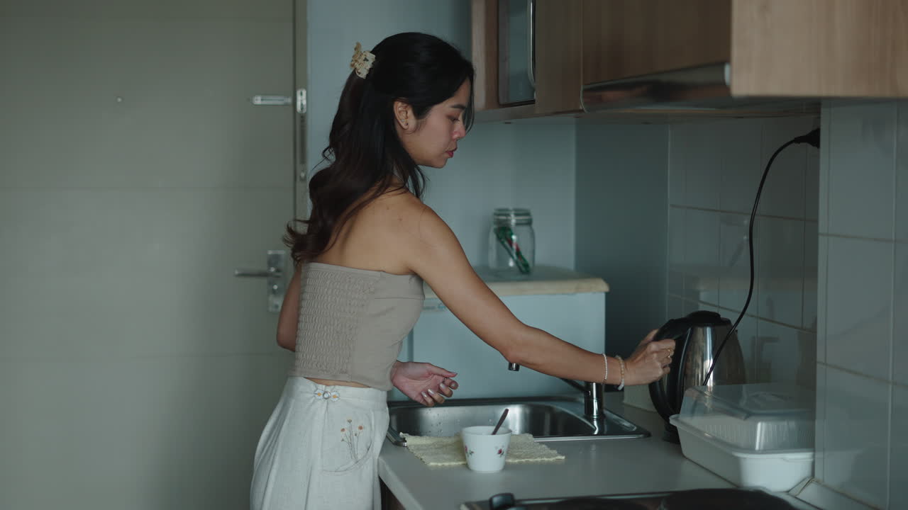 キッチンでコップに水を注ぐ女性