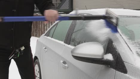 a man scraping layers of ice build-up on the roof of his car - medium shot