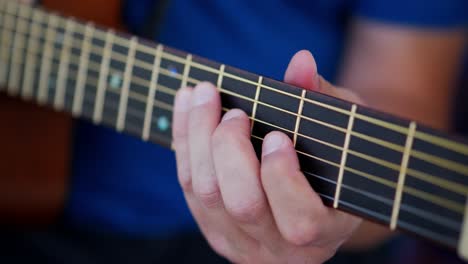 dedos de un hombre blanco caucásico con camisa azul tocando una guitarra acústica cerca de la parte superior del tablero de trastes