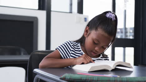 In-Einem-Schulklassenzimmer-Ist-Ein-Junges-Mädchen-Mit-Gemischter-Abstammung-Auf-Das-Lesen-Eines-Buches-Konzentriert