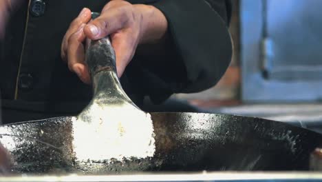 chef cleaning big pan with water and wooden brush