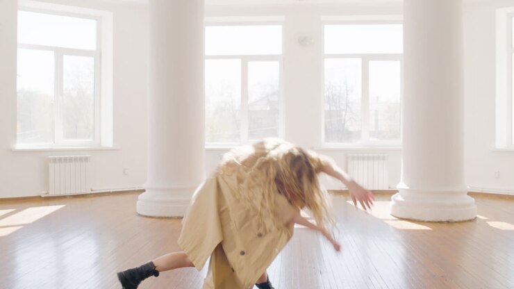 Focused Blonde Woman In Trench Coat And Boots Training A Contemporary Dance In The Middle Of The Studio 3
