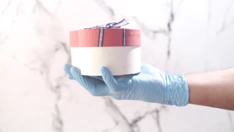 hand in gloves holding a heart-shaped gift box