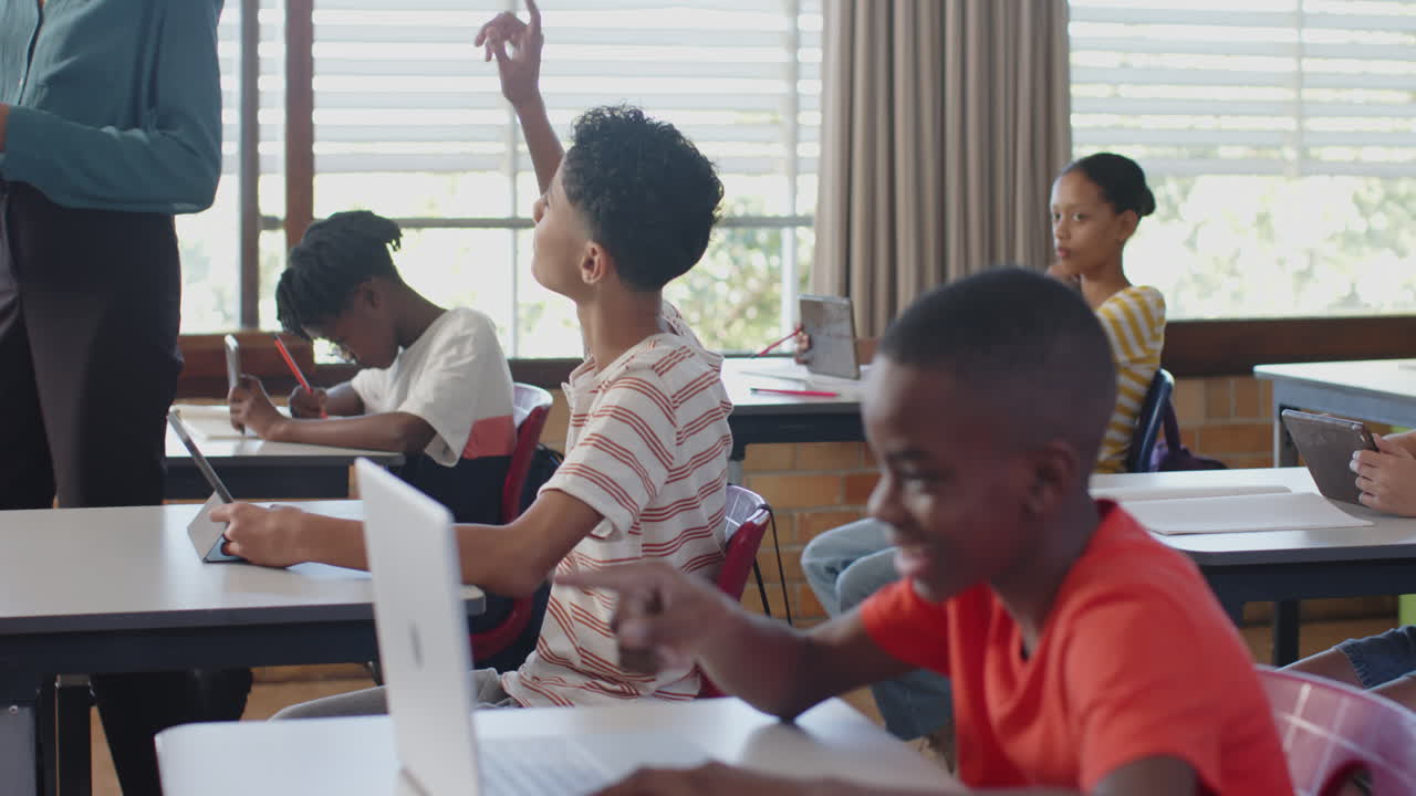 In school, students using laptops and tablets in classroom with teacher assisting